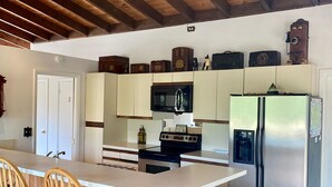 Een keuken met houten balken, een centraal eiland met barstoelen, een koelkast en een magnetron.