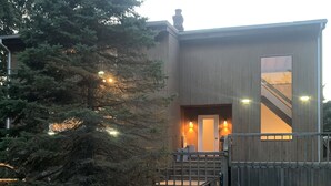 Een modern huis met een houten gevel, een pad van stenen naar een zwembad, en een grote boom in de achtertuin.