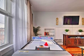 Taula de ping-pong a un saló amb una finestra gran, una prestatgeria i un televisor penjat a la paret.