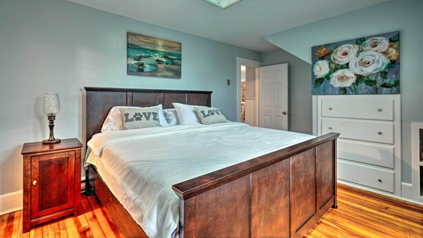 Een slaapkamer met een houten bed, een nachtkastje met een lamp, een schilderij aan de muur en een dressoir.
