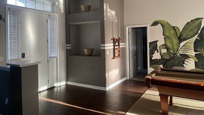 A room with a wooden floor, a pool table, a large plant, and a built-in shelving unit with a bowl on top. - Gorgeous Heated Pool Home Built in 2020 with Jacuzzi- 5.3 mi from INTL Airport…  (Jacksonville)
