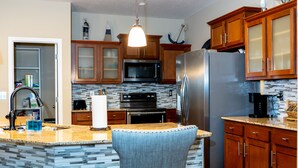 A kitchen with granite countertops, wooden cabinets, a stainless steel refrigerator, a microwave, and an island with a chair. - Gorgeous Heated Pool Home Built in 2020 with Jacuzzi- 5.3 mi from INTL Airport…  (Jacksonville)