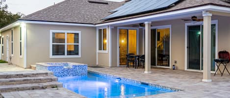 Una casa con piscina, patio y paneles solares en el tejado.