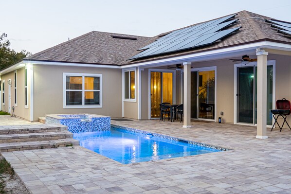 A house with a swimming pool, patio, and solar panels on the roof.