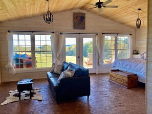 A spacious room with a blue sofa, a wooden chest, and a cowhide rug. - One room cabin set on our farm for a peaceful getaway. (Union Hall)