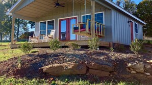 A single-story house with a porch, a swing, and a red door. - One room cabin set on our farm for a peaceful getaway. (Union Hall)