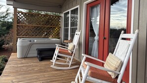 A covered deck with two rocking chairs and a hot tub. - One room cabin set on our farm for a peaceful getaway. (Union Hall)