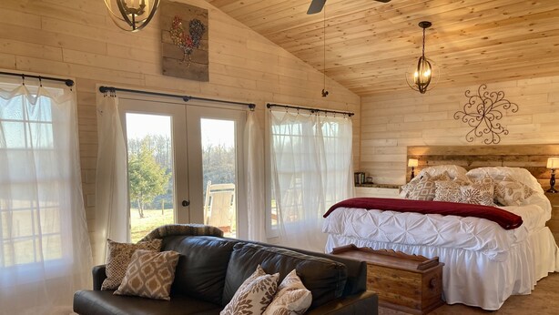 A cozy room with a leather sofa, a large bed with white bedding, and a wooden ceiling. - One room cabin set on our farm for a peaceful getaway. (Union Hall)