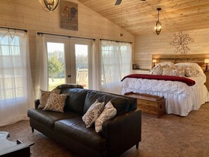 A cozy room with a leather sofa, a large bed with white bedding, and a wooden ceiling.