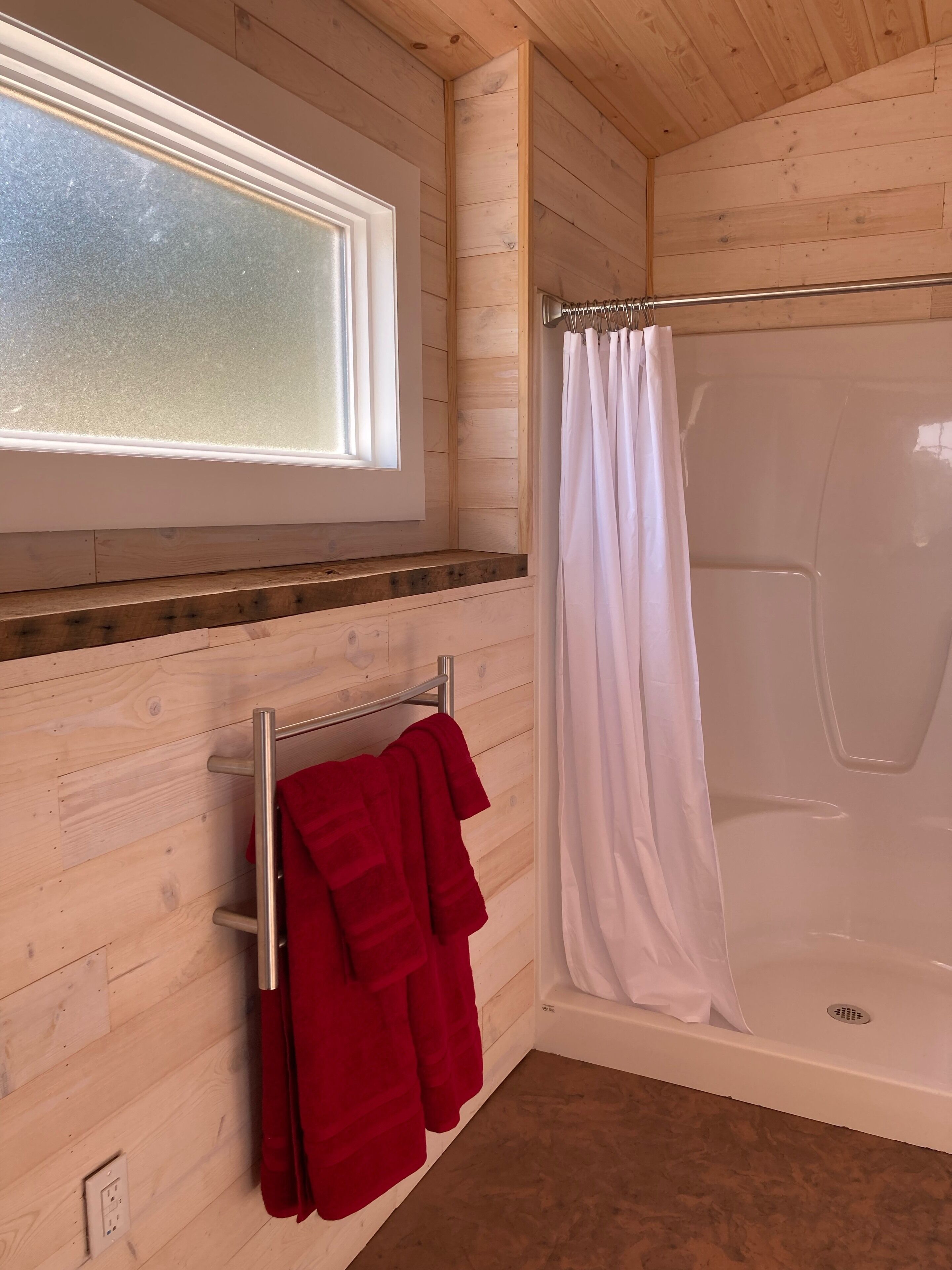 Ein Holzinnenraum mit einer Badewanne, einem Fenster und einem Handtuchhalter mit roten Handtüchern.