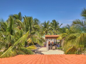 A beachside resort with a covered seating area, palm trees, and a sandy path leading to the beach. - Casa Macabi - Yucatan Home Rentals (Chicxulub Puerto)