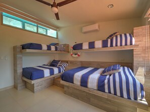 A bunk bed room with a ceiling fan, an air conditioning unit, and a window with a view. - Casa Macabi - Yucatan Home Rentals (Chicxulub Puerto)