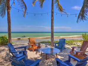A beachside seating area with chairs and a table, overlooking a clear blue sea. - Casa Macabi - Yucatan Home Rentals (Chicxulub Puerto)