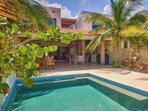 A swimming pool with a tiled edge, surrounded by lounge chairs and a patio area with a thatched roof. - Casa Macabi - Yucatan Home Rentals (Chicxulub Puerto)