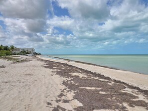 A beach with a clear view of the ocean and a building in the background. - Casa Macabi - Yucatan Home Rentals (Chicxulub Puerto)