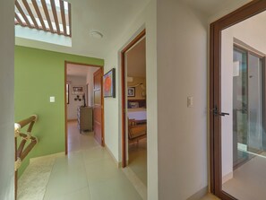 A hallway with a wooden chair, a bed with a blue headboard, and a door leading to a balcony. - Casa Macabi - Yucatan Home Rentals (Chicxulub Puerto)