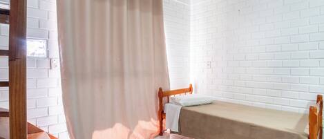 A small, clean room with white brick walls, a wooden bed frame, and a single bed with a beige cover.