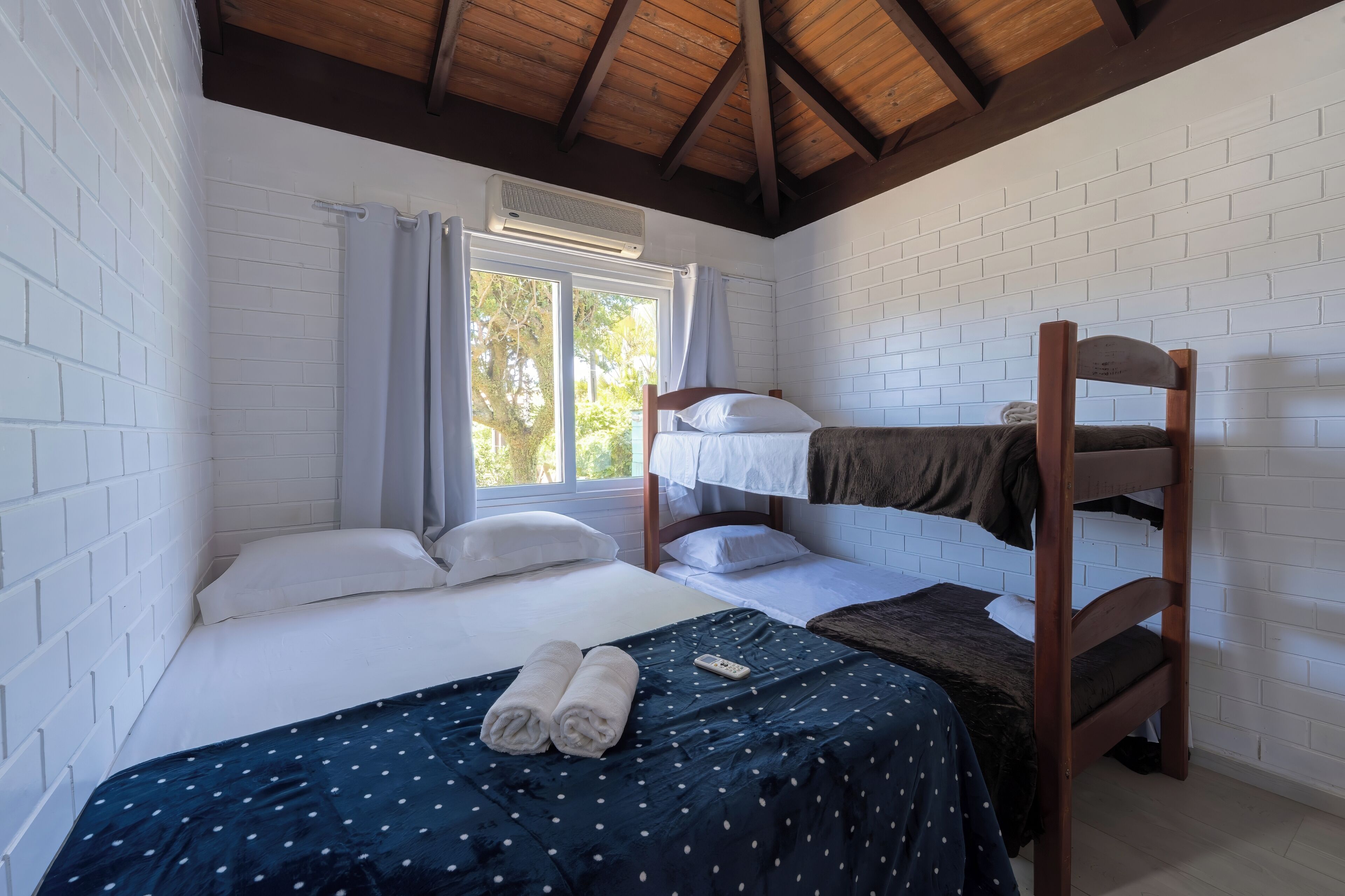 Quarto com beliche, uma cama de solteiro e janela com cortinas.