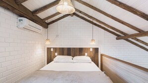 A bedroom with a wooden headboard, white brick walls, and a sloped ceiling with exposed beams.