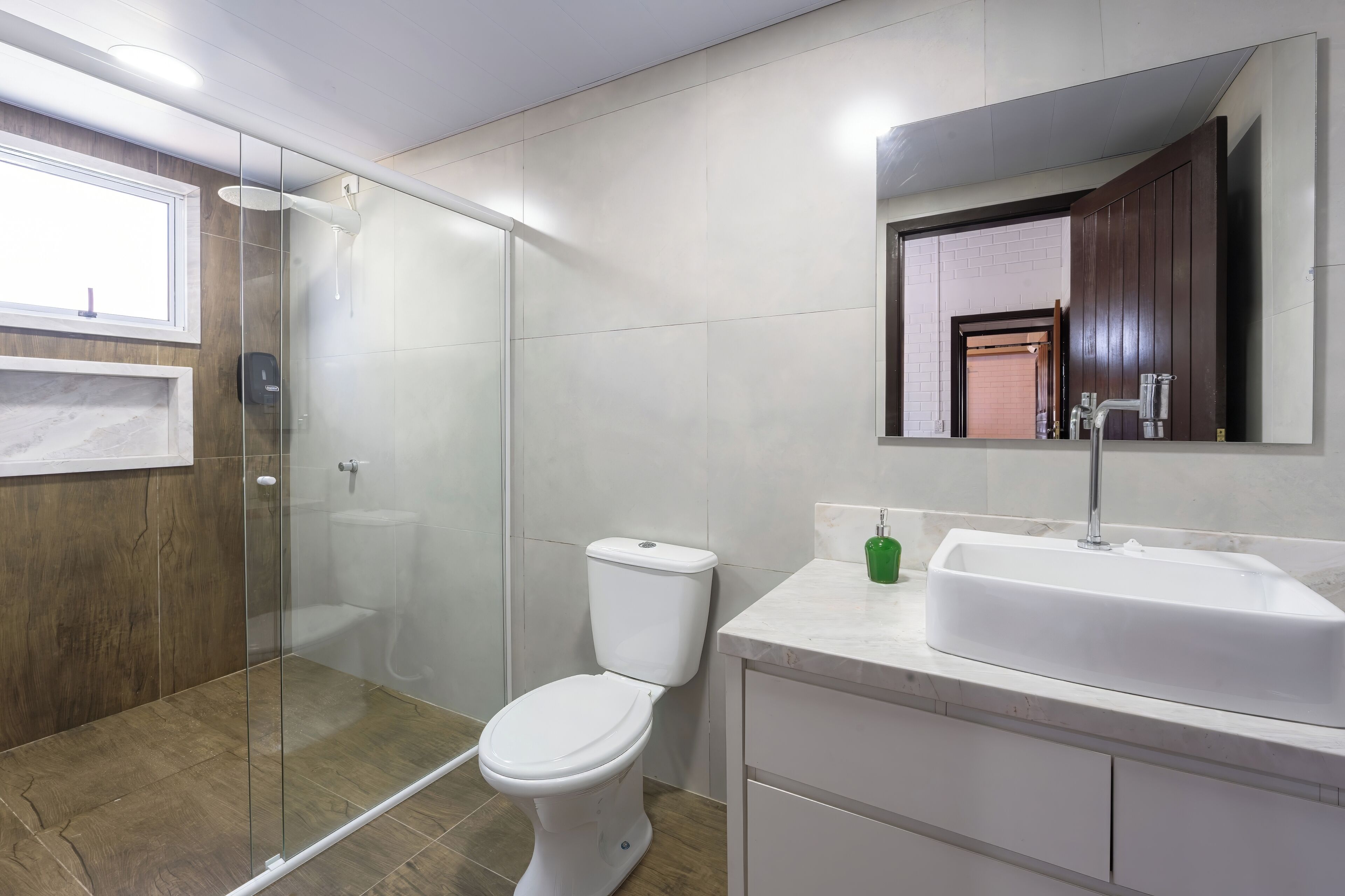 A modern bathroom with a glass-enclosed shower, a white toilet, a marble sink, and a wooden vanity.