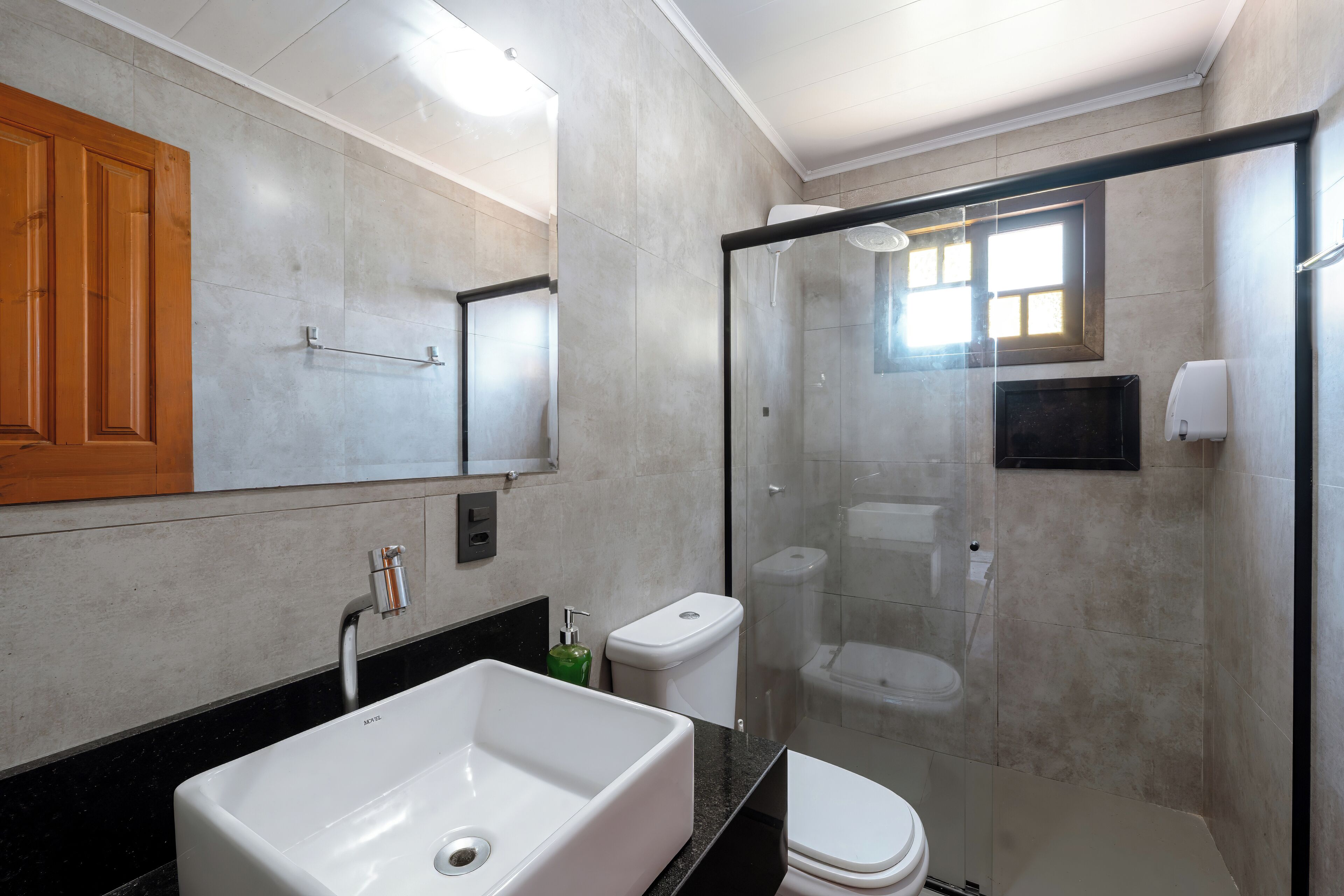 Un baño moderno con un lavamanos blanco grande, un inodoro y una ducha con cerramiento de vidrio.