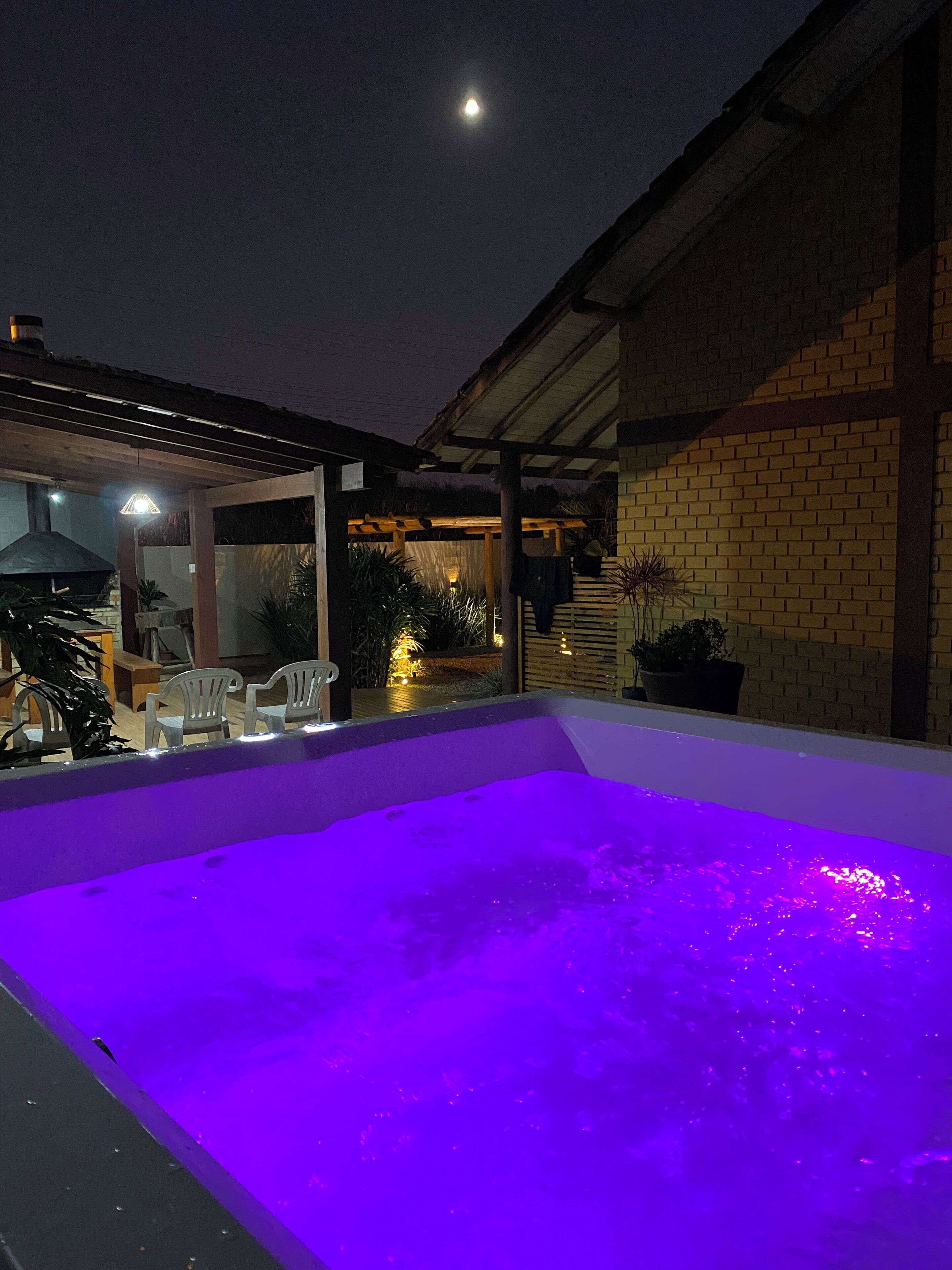 A swimming pool with a purple light, a covered patio area, and a brick building in the background.