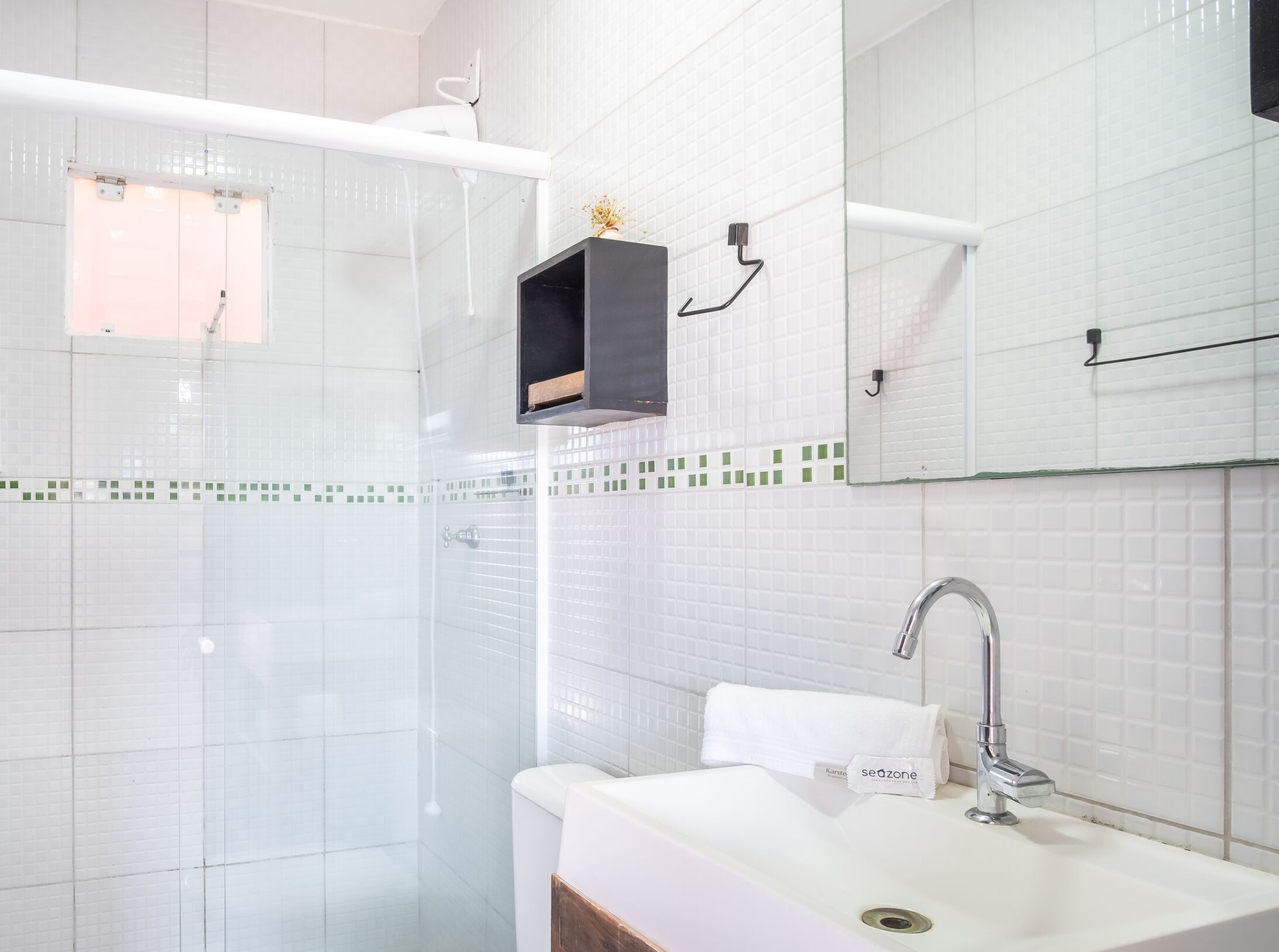 A modern bathroom with a glass-enclosed shower, a white sink with a towel, and a mirror with a towel hanging on it.