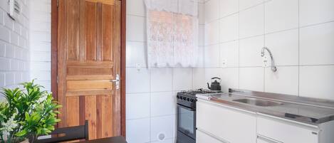 A kitchen with white tiled walls, a wooden door, a stove, a sink, and a vase with green plants.