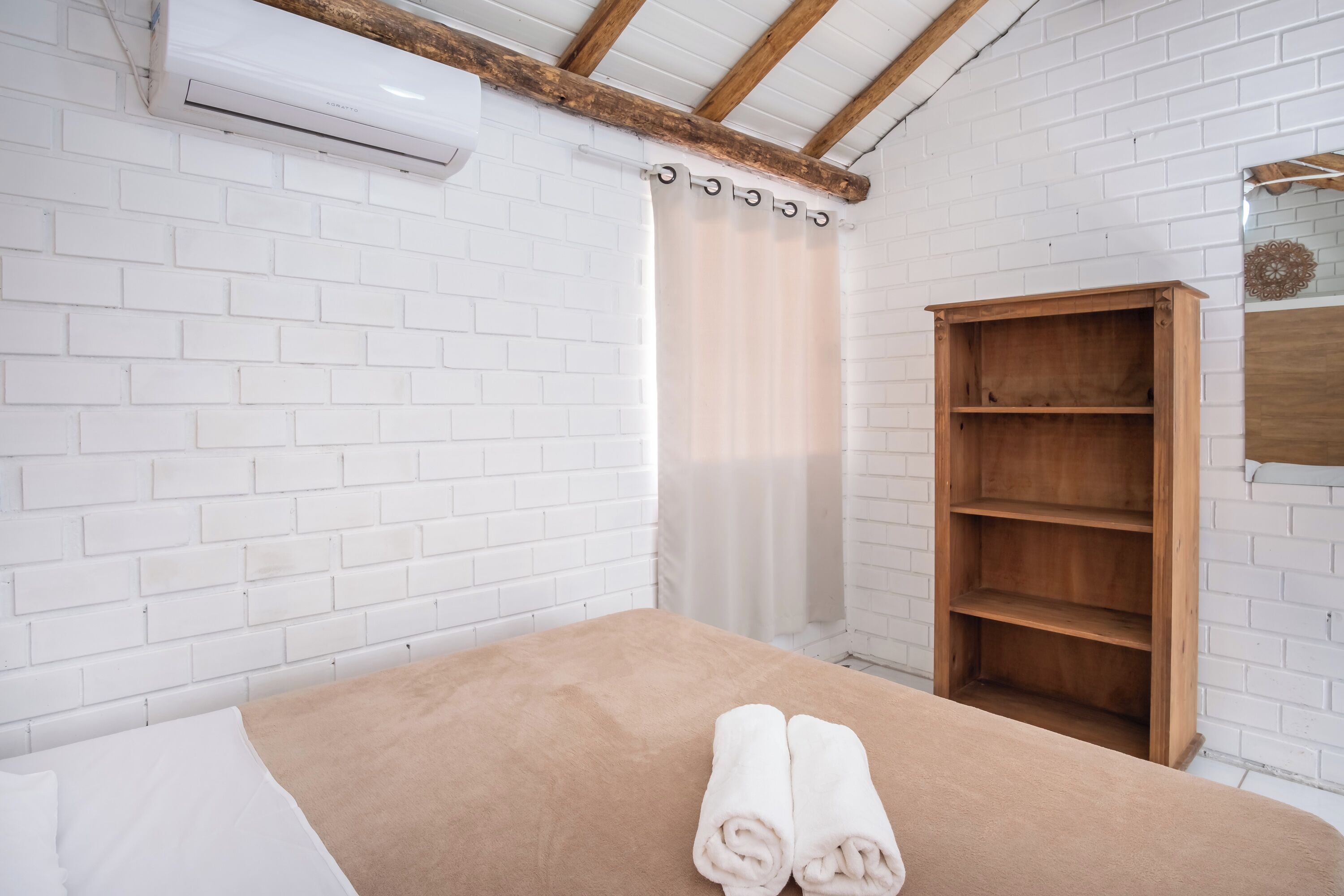 Une pièce avec un lit, une étagère en bois et un mur en briques blanches.