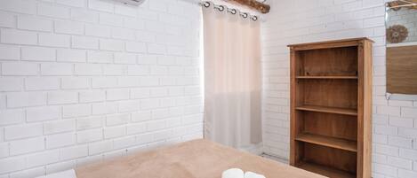 A room with a bed, a wooden shelf, and a white brick wall.