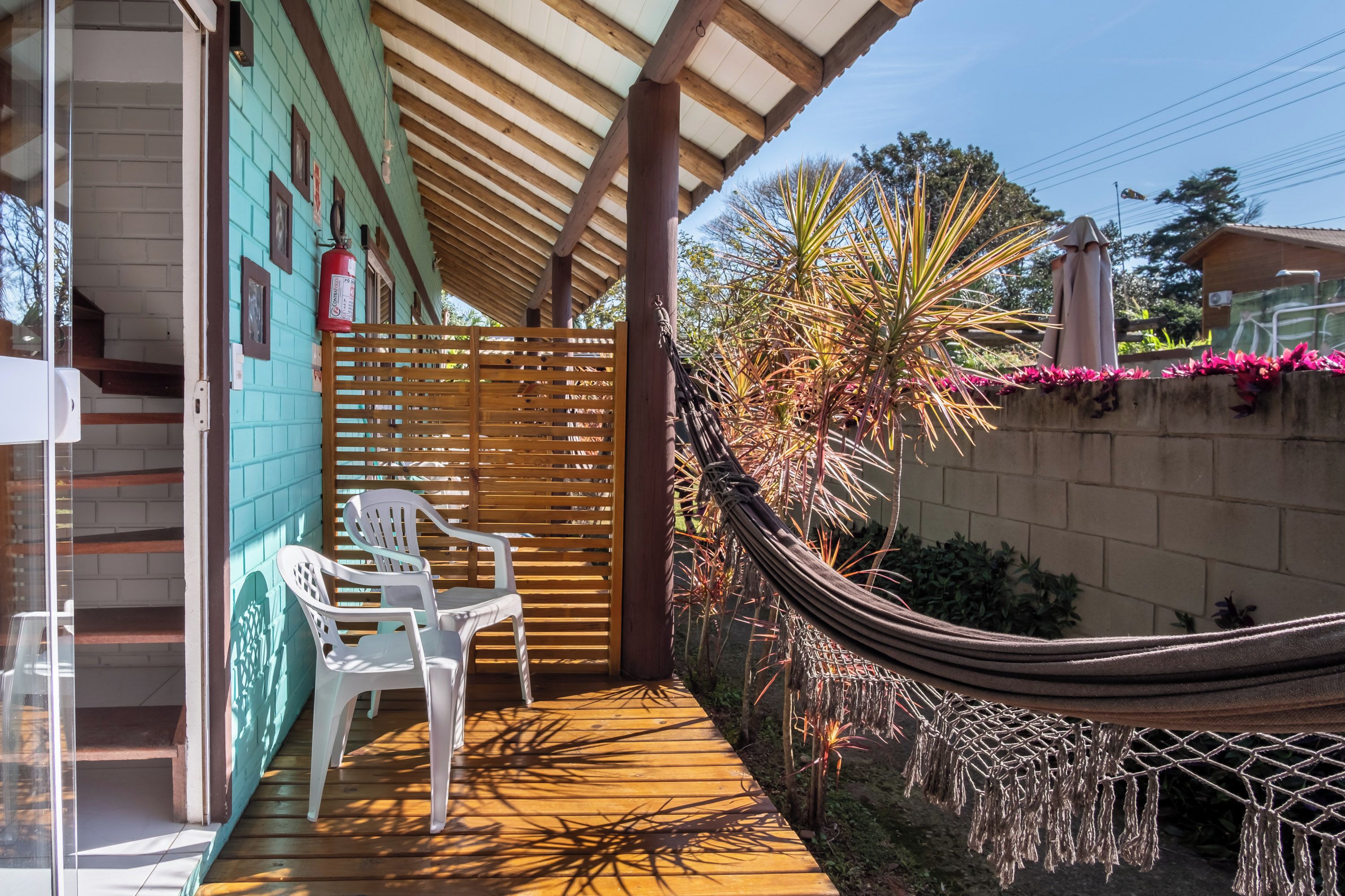 A wooden deck with a hammock, white plastic chairs, and a wooden fence.