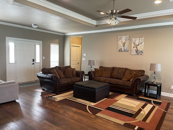 A living room with a brown leather sofa, a matching ottoman, two side tables with lamps, a ceiling fan, and a patterned rug. - Beautiful 8.5 acres farm house with sunroom and basketball court (Pilot Point)