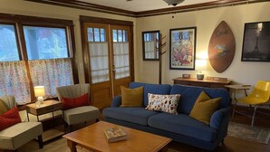 A living room with a blue sofa, a wooden coffee table, and a patterned rug. There are two armchairs, a small table with a lamp, and a framed picture on the wall. - Historic and unique home on the hill, blocks away from the Marietta Square. (Marietta)