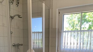 A bathroom with a glass-enclosed shower, a toilet, and a window with a view of greenery. - Wiesenblick - Idyllic and quiet location, family-friendly (Grube)