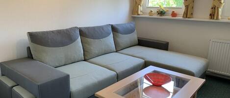 Una sala de estar moderna con un sofá seccional gris, una mesa de centro de vidrio y una ventana con cortinas.