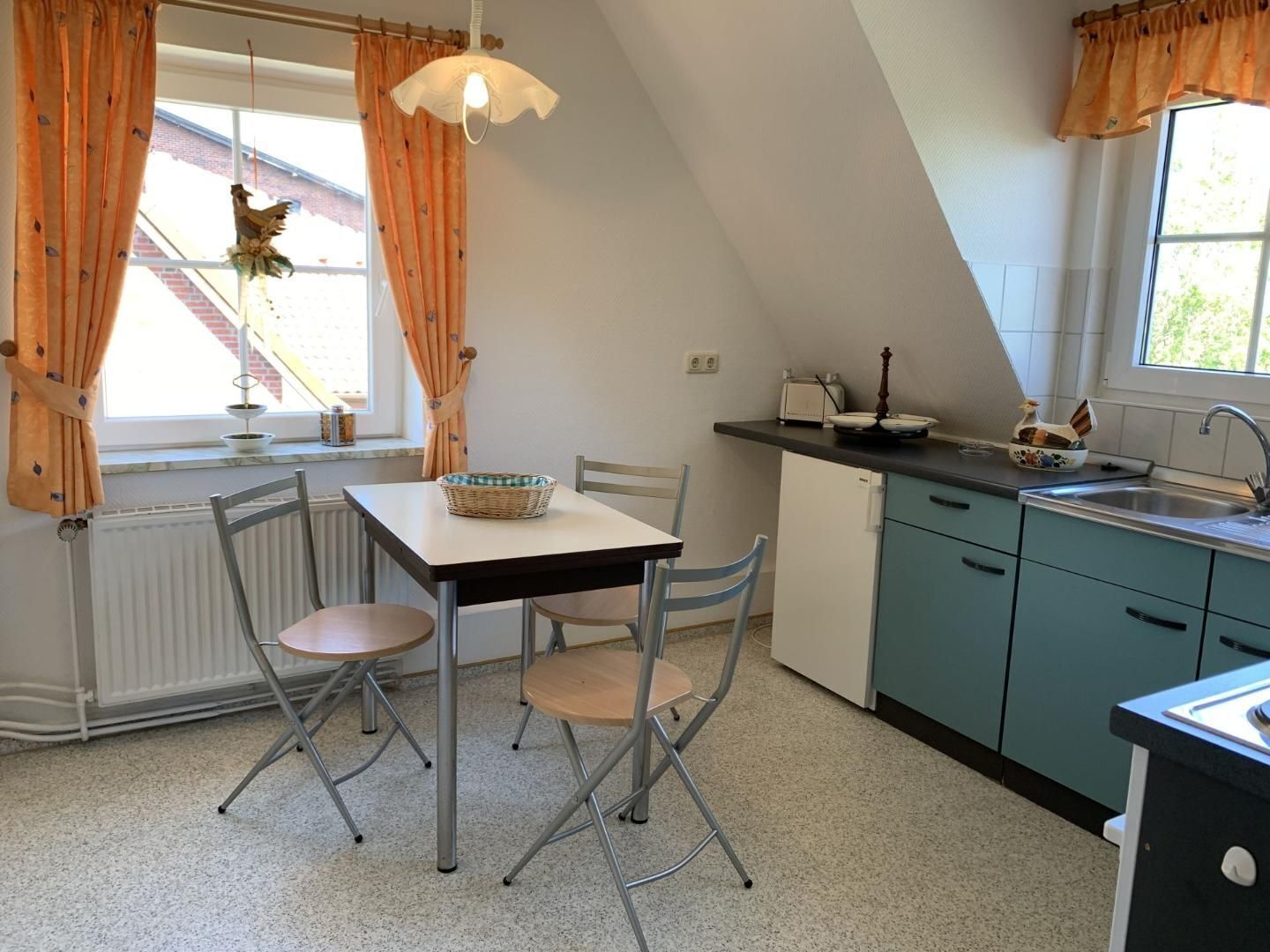 A kitchen with a dining table, chairs, a radiator, a window with curtains, and a sink.
