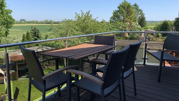 En terrasse med et bord og stole, der udover et grønt landskab.