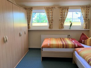 Een slaapkamer met een eenpersoonsbed, een kledingkast en een raam met gordijnen.