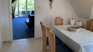 En spiseplads med et bord dækket til to, en lysekrone og udsigt til et udendørs siddeområde gennem en glasdør.