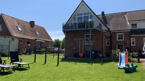 Et boligområde med græsplæne, gyngestativ, rutschebane og en murstensbygning med balkon.