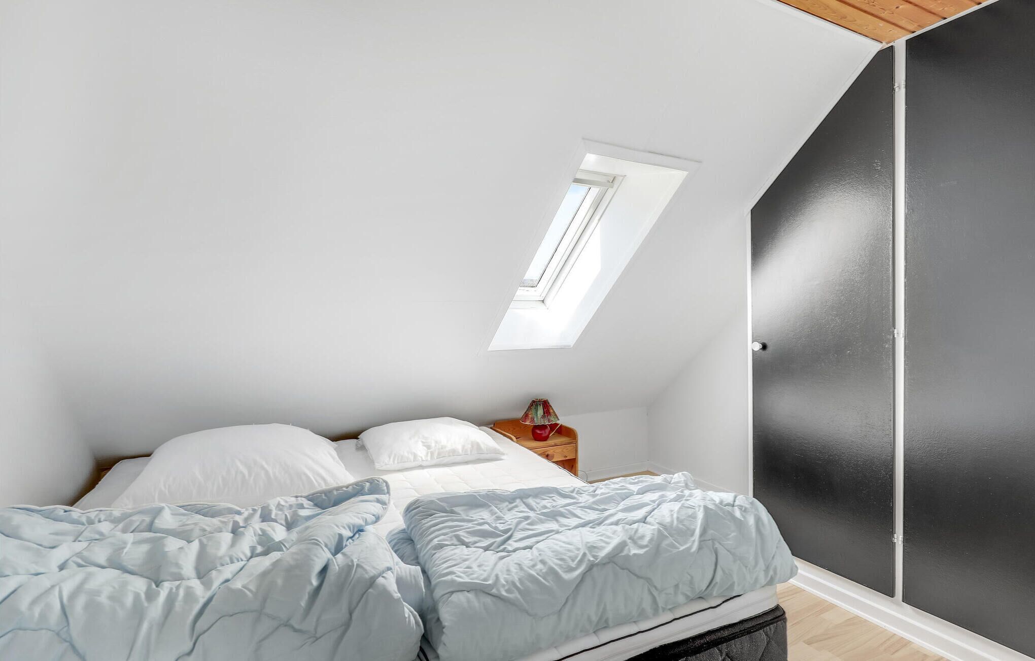 Une chambre à coucher avec un lit, une table de chevet, une lampe, une fenêtre et une porte.
