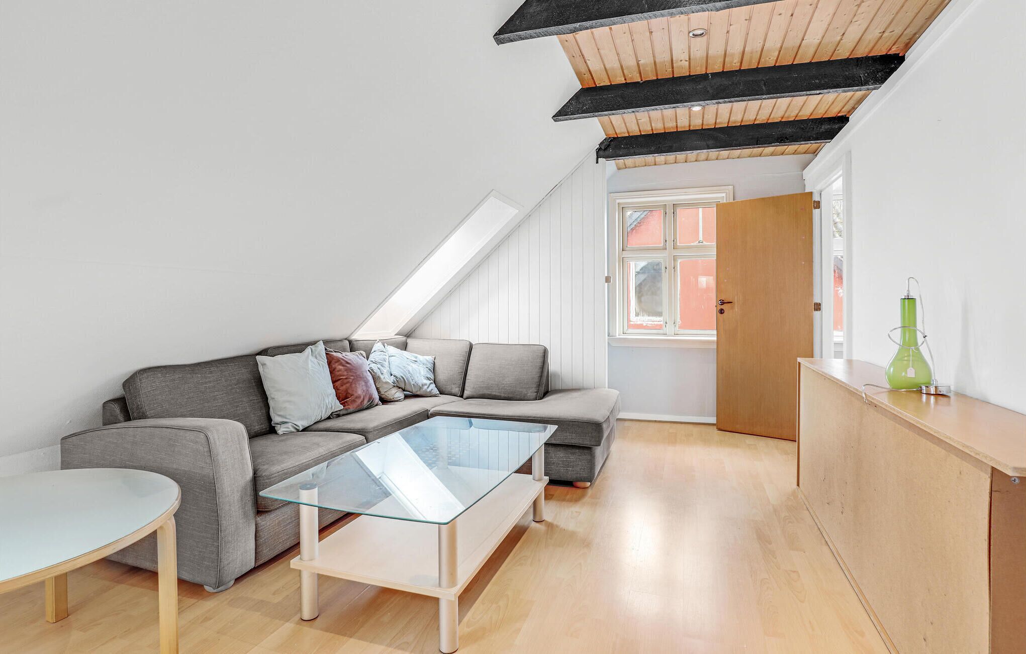 Un moderno apartamento tipo loft con cama alta, un sofá seccional gris, una mesa de centro de vidrio y un banco de madera.