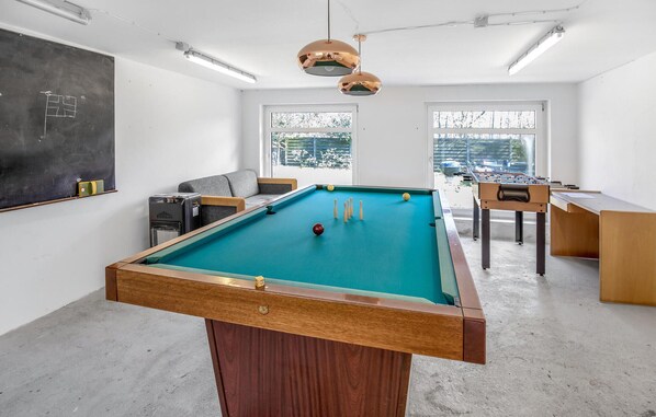 A pool table in a room with a chalkboard, windows, and a foosball table.