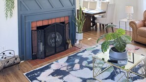 Ein Wohnzimmer mit Kamin, einem an der Wand montierten Fernseher, einer Kristallleuchtre und einem Essbereich mit Tisch und Stühlen.