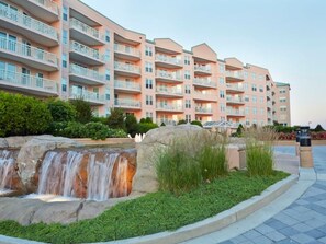 A multi-story hotel with balconies, a landscaped garden with a small waterfall, and a paved walkway. - The Jersey Shore's Premier Oceanfront Resort (Wildwood Crest)