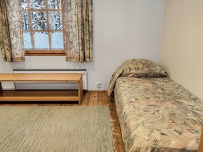A small, sparsely furnished room with a bed, a bench, and a window with curtains. - Vacation home Koivu by Interhome (Kuusamo)