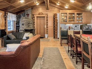 A cozy cabin interior with a living area, wooden walls, a stone fireplace, and a kitchen with wooden cabinets. - Vacation home Koivu by Interhome (Kuusamo)