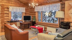 A cozy log cabin interior with a leather sofa, a red table, and a television.