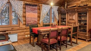 A cozy log cabin interior with a wooden dining table, chairs, a bookshelf, and a fireplace.