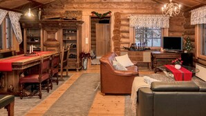 A cozy log cabin interior with a dining area, a leather sofa, and a television.
